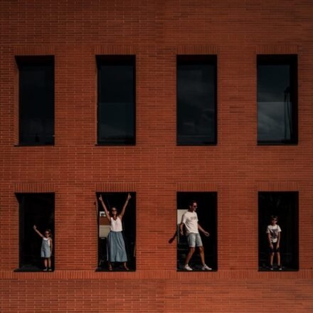 Famille de quatre personnes posant devant la façade graphique d'un bâtiment en brique, créant une composition visuelle forte
