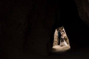 Mariés enlacés dans la lumière, vus depuis l'intérieur d'une grotte des Bardenas Couple de mariés s'enlaçant, parfaitement éclairés à l'entrée d'une grotte, vue depuis l'intérieur sombre de la cavité dans le désert des Bardenas